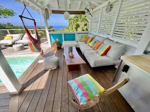 Una terraza de madera con sofá, reposapiés y sillón, una silla colgante, y vista al océano.