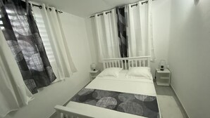 Ein Schlafzimmer mit einem weißen Bett, zwei Nachttischen, einem Fenster mit Vorhängen.