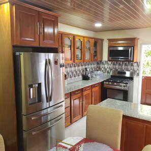 A kitchen with wooden cabinets, stainless steel appliances, and a tiled backsplash. - Veron's Country Getaway<br><br>TUSCHEN West Coast Demerara (Tuschen, East bank Essequibo)