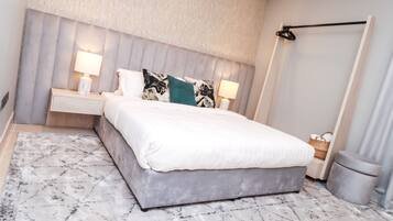 A modern bedroom with a large bed, two bedside tables with lamps, a grey headboard, and a patterned rug.