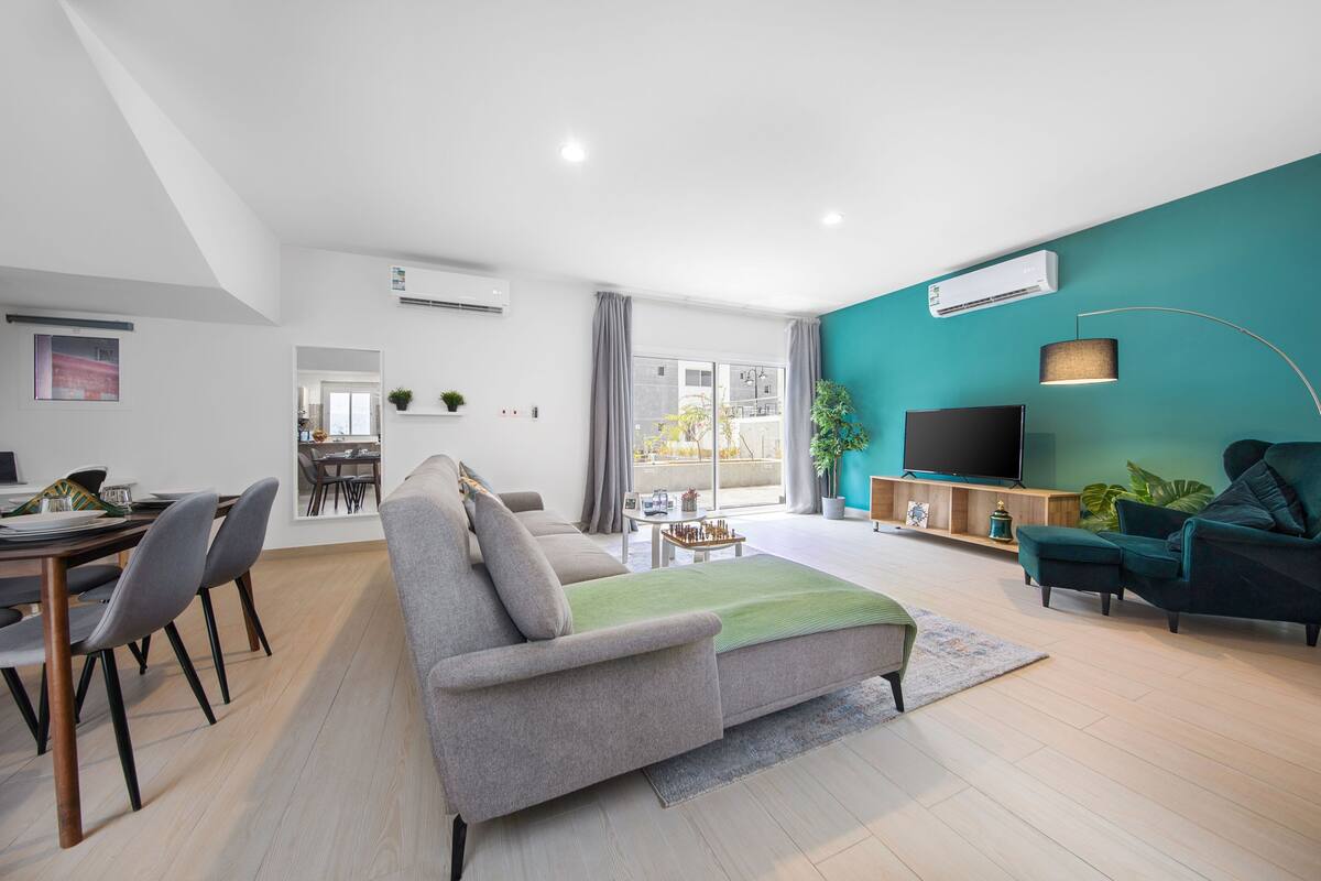 A modern living room with a grey sofa, a teal accent wall, and a flat-screen TV.