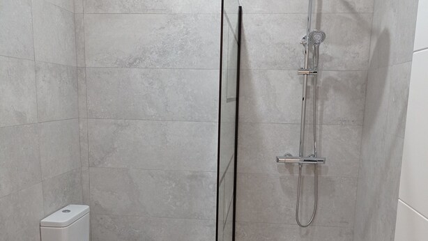 A modern bathroom with a glass-enclosed shower, a toilet, and a vanity with a mirror. - URDAIHOME APARTMENT (Gernika-Lumo)