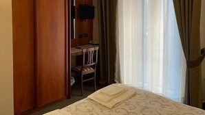A hotel room with a bed, a desk with a chair, a television, and a wardrobe.
