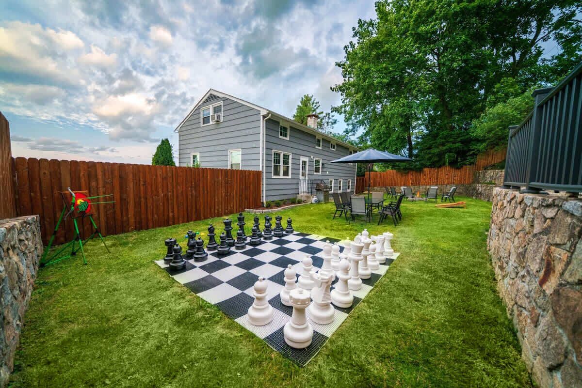 A backyard with a large checkered game board, a wooden fence, and a house in the background.