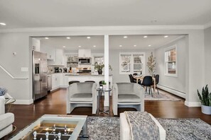 A spacious living area with a foosball table, a dining area with a table and chairs, and a kitchen with modern appliances. - Waterview House Walking Distance from Cove Beach (Stamford)