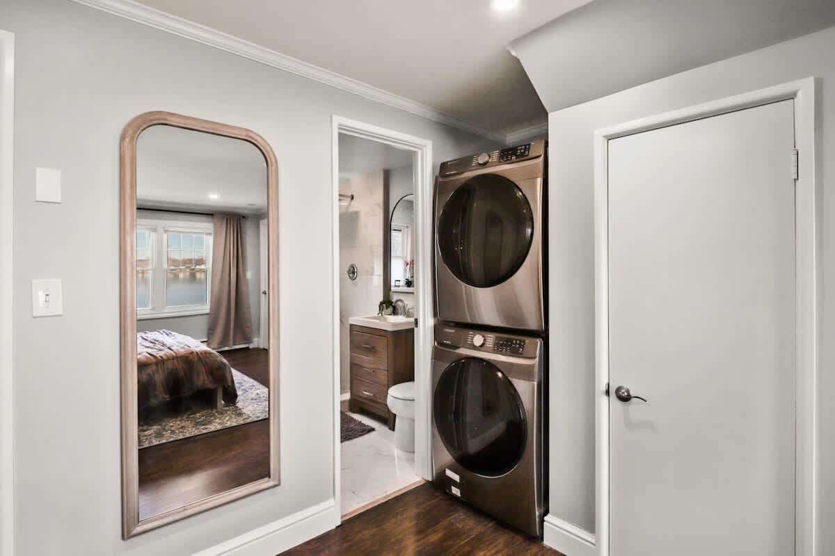 A compact bedroom with a large mirror, a bed, and a walk-in closet with a washing machine.
