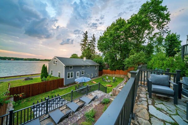 A residential backyard with a stone patio, outdoor furniture, a wooden fence, and a view of a lake. - Waterview House Walking Distance from Cove Beach (Stamford)