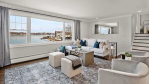A spacious living room with a large window, a sofa set, a coffee table, and a view of a body of water. - 5BR Beach House, Water Views, Game Room, Backyard (Stamford)