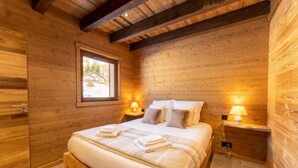 A wooden room with a bed, two bedside tables with lamps, and a window. - Luxury chalet LE CARIBOU, near Gérardmer, exceptional view, jacuzzi. (Xonrupt-Longemer)