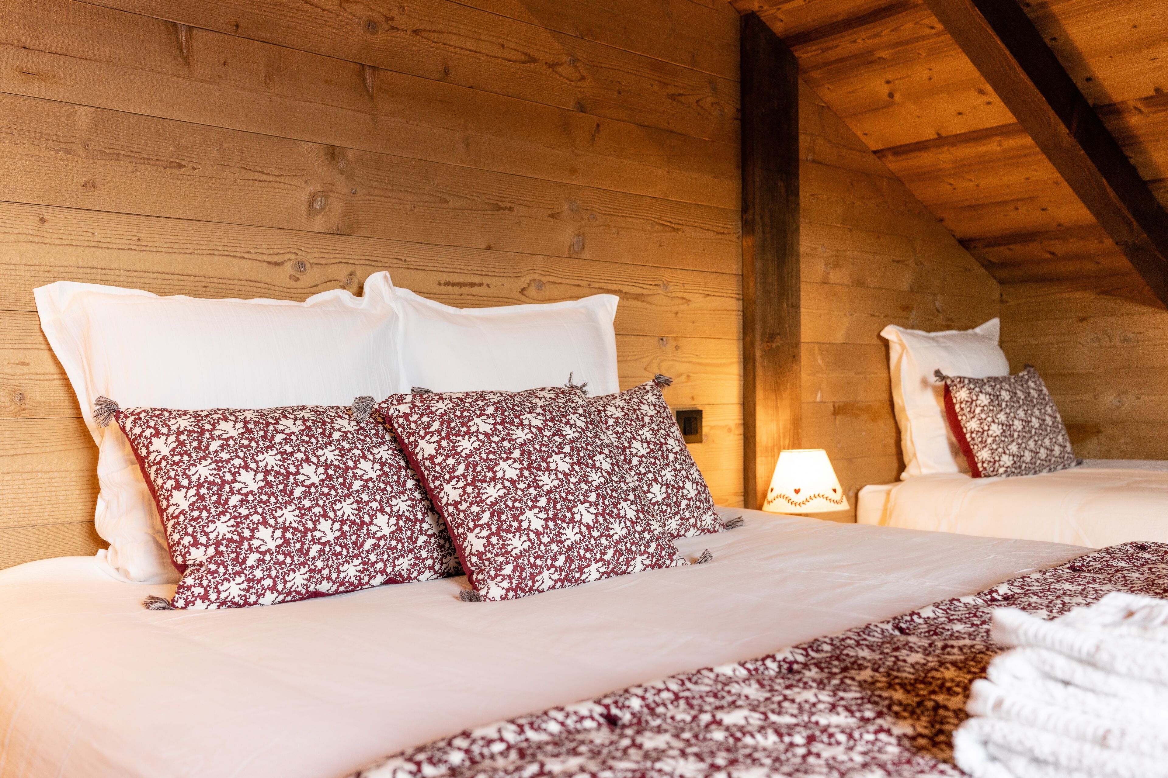 Un dormitorio de cabaña de madera acogedor, con cama, almohadas y una mesita de noche con lámpara.