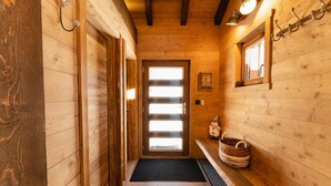 A wooden interior hallway with a door leading to a bright room, a bench with baskets, and wall-mounted hooks. - Luxury chalet LE CARIBOU, near Gérardmer, exceptional view, jacuzzi. (Xonrupt-Longemer)