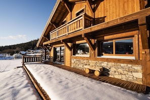 A wooden cabin with a stone foundation, large windows, and a wooden deck.