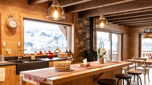 A wooden interior with a kitchen area, bar stools, and large windows with a snowy view. - Luxury chalet LE CARIBOU, near Gérardmer, exceptional view, jacuzzi. (Xonrupt-Longemer)
