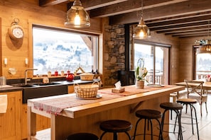 A wooden interior with a kitchen area, bar stools, and large windows with a snowy view.
