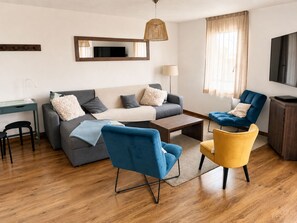 Una sala de estar moderna con un sofá, dos sillones, una mesa de centro, un televisor y piso de madera.