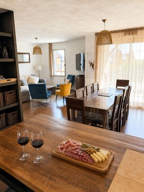 A dining area with a wooden table set for two, a charcuterie board with meats and cheeses, and two wine glasses.