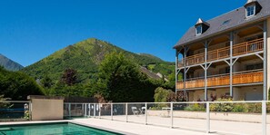 A hotel with a pool, wooden balconies, and a mountain backdrop.