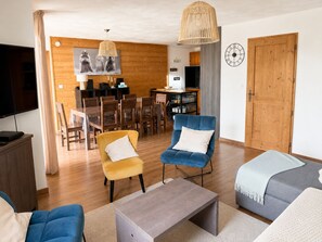 Una sala de estar con televisor, dos sofás, una mesa de centro y un comedor con mesa y sillas.