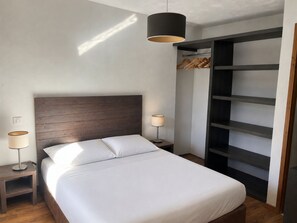A bedroom with a wooden headboard, a bed with white bedding, two bedside lamps, and a built-in shelving unit.
