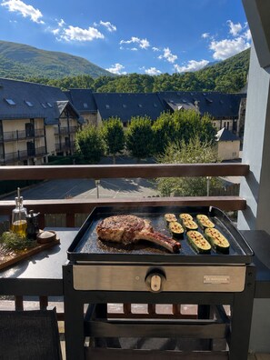 Una parrilla con un bistec y medio zucchini en un balcón con vistas a un barrio residencial con casas y árboles.