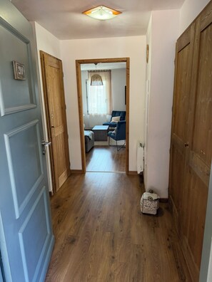 A hallway leading to a living area with a sofa and a table, wooden flooring, and a ceiling light.