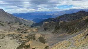 Eine gebirgige Landschaft mit einem Tal und fernen Bergreihen unter bewölktem Himmel.