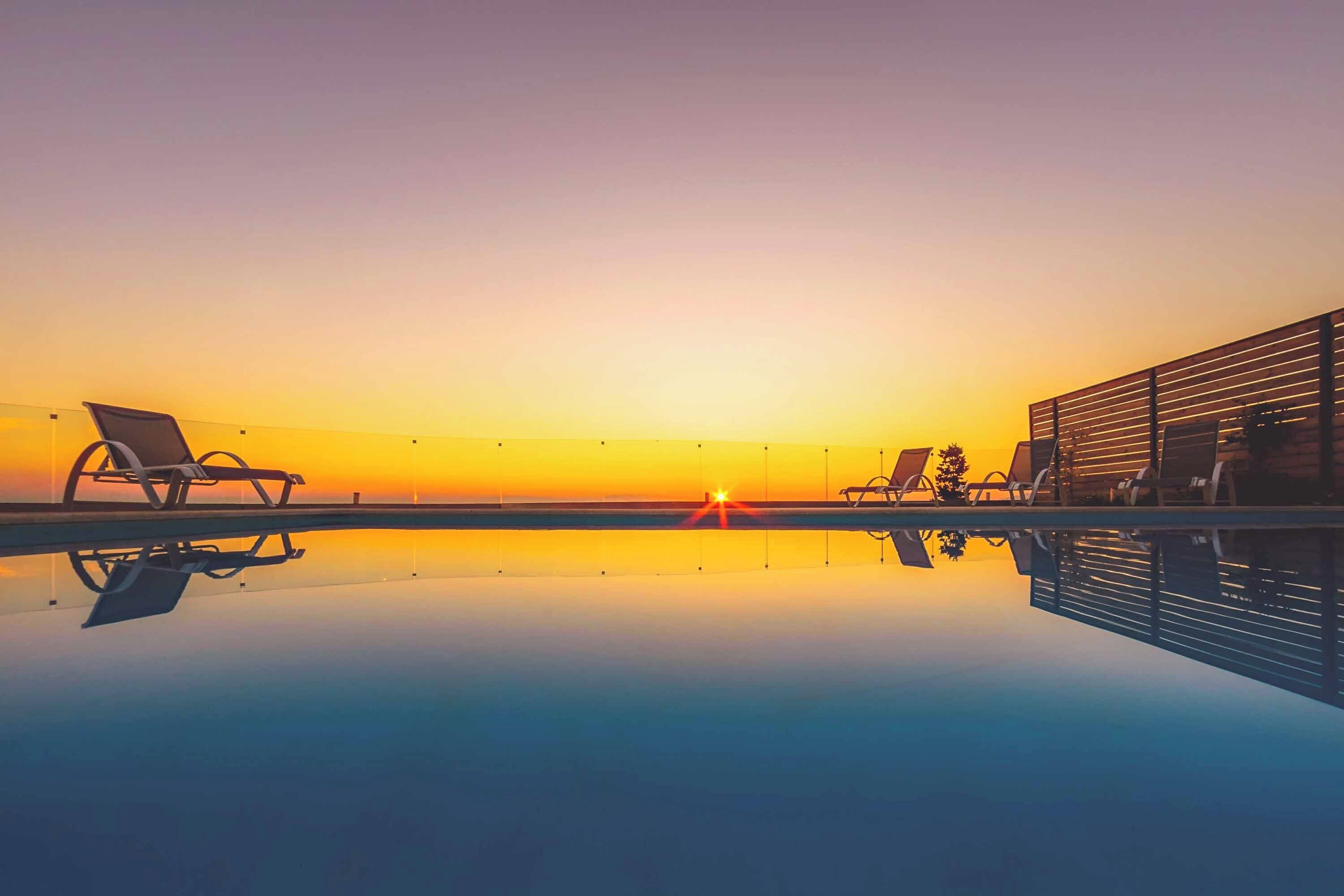 A serene poolside view at sunset with lounge chairs and a wooden deck.