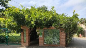 Une entrée de jardin agrémentée d’une arche en briques et d’une enseigne indiquant « Le Jardin des Plantes des Capellans ».