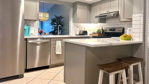A modern kitchen with stainless steel appliances, a large island, and a dining area with stools. - Serene Resort-style Villa minutes to Siesta Key, in popular Village des Pins (Sarasota)