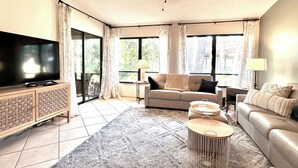 A living room with a flat-screen TV, a sofa, a coffee table, and a ceiling fan. - Serene Resort-style Villa minutes to Siesta Key, in popular Village des Pins (Sarasota)