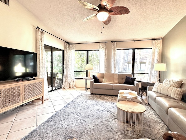 A living room with a flat-screen TV, a sofa, a coffee table, and a ceiling fan.