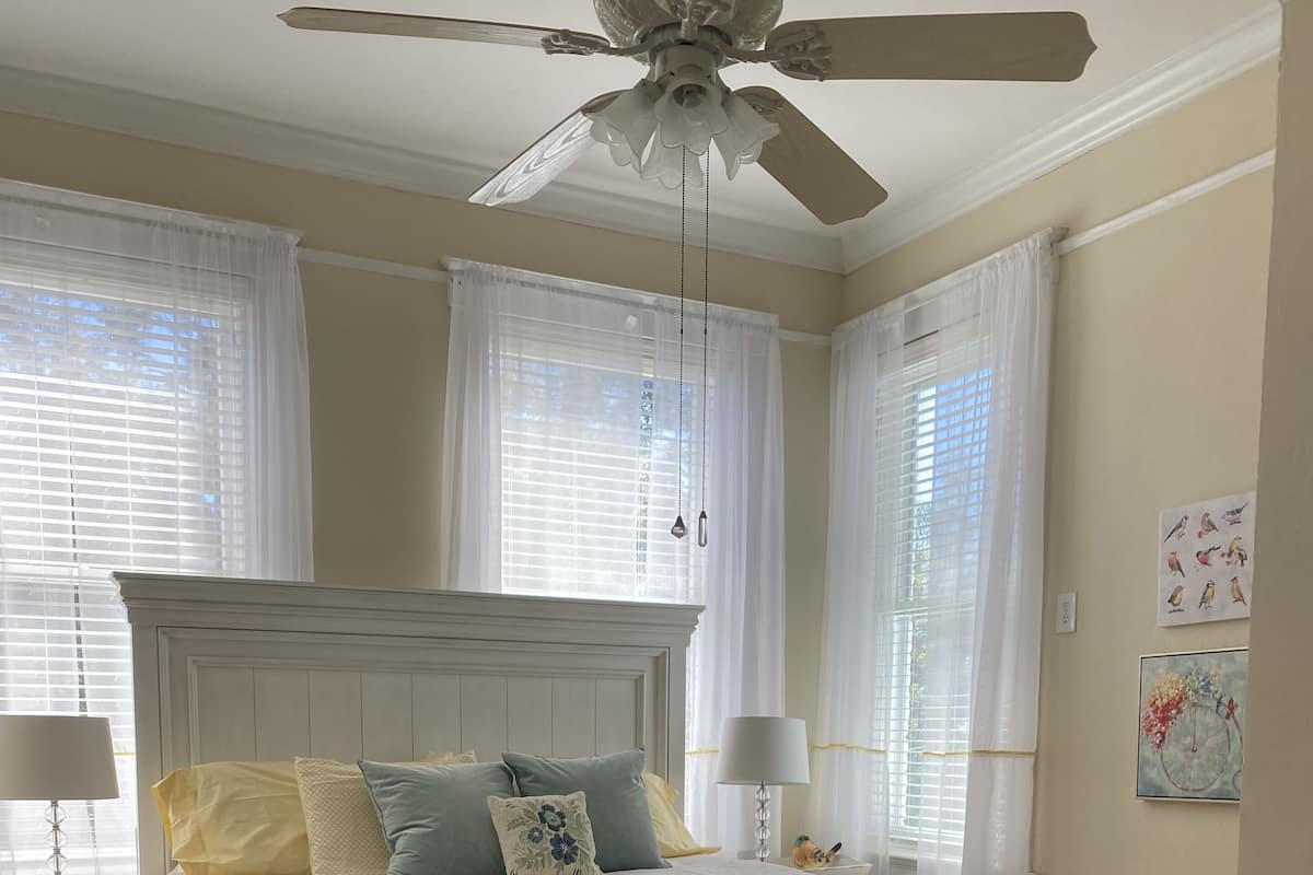 A bedroom with a large bed, two bedside tables, a ceiling fan, and a window with curtains.