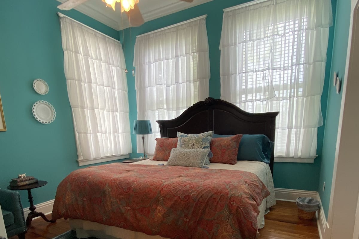 A bedroom with a bed, a ceiling fan, and a window with sheer curtains.