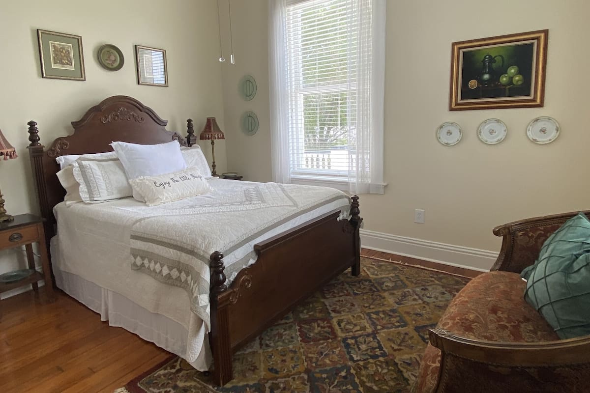 A bedroom with a wooden bed, a ceiling fan, a window with blinds, and a rug.