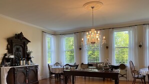 Comedor con candelabro, muebles de madera y ventanas amplias con cortinas.