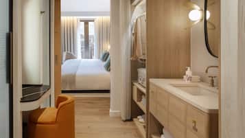 A hotel room with a bed, a bathroom with a sink and mirror, and a view of the city through the window.