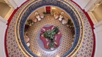 A grand circular staircase with ornate railings, a central seating area with cushions and plants, and a patterned floor.