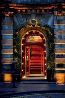 Egy szálloda bejárata, piros ajtóval, díszes ívekkel és egy „Virgin Hotels” felirattal ellátott táblával.