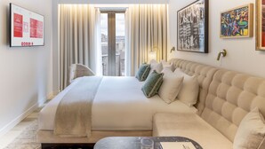 A hotel room with a large bed, a sofa, a flat-screen TV, and artwork on the walls.