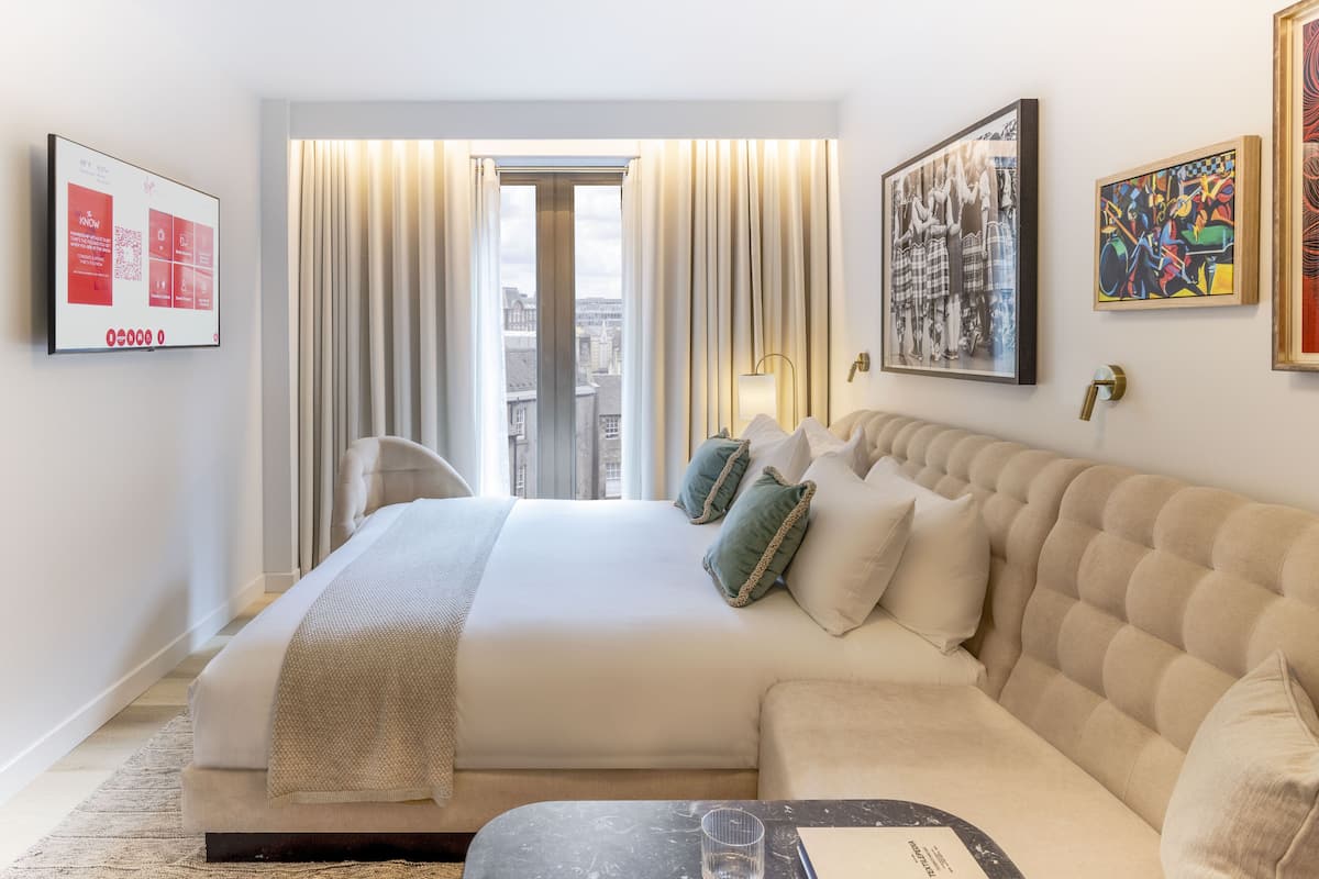 A hotel room with a large bed, a sofa, a flat-screen TV, and artwork on the walls.