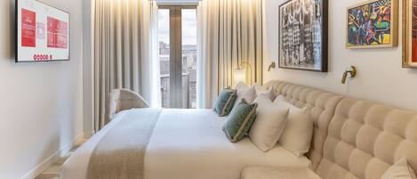 A hotel room with a large bed, a sofa, a flat-screen TV, and artwork on the walls.