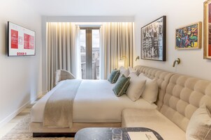 A hotel room with a large bed, a sofa, a flat-screen TV, and artwork on the walls.