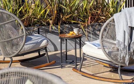 A rooftop terrace with wicker chairs, a small table with a cup and snacks, and a view of a castle-like building in the background.