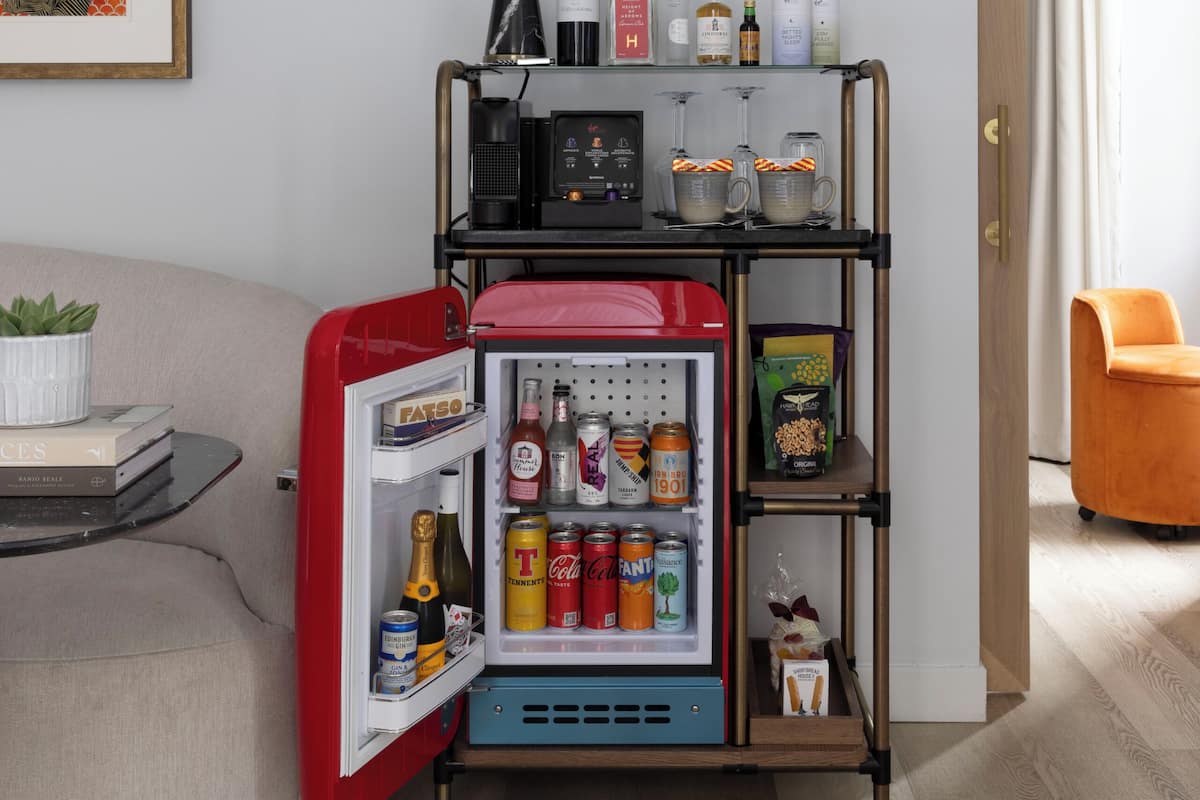 A compact living space with a kitchenette, a fridge, a small table with a plant, and a door leading to another room.