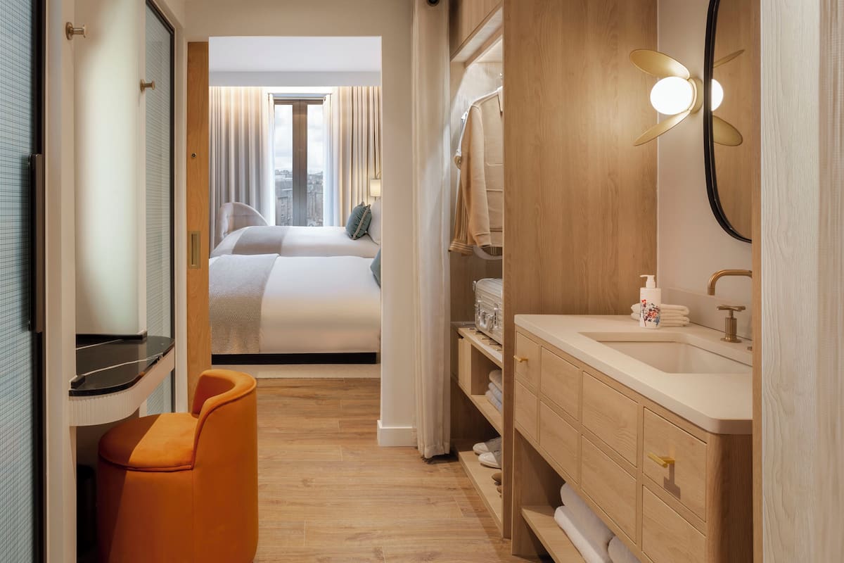 A hotel room with a bed, a bathroom with a sink and mirror, and a chair.