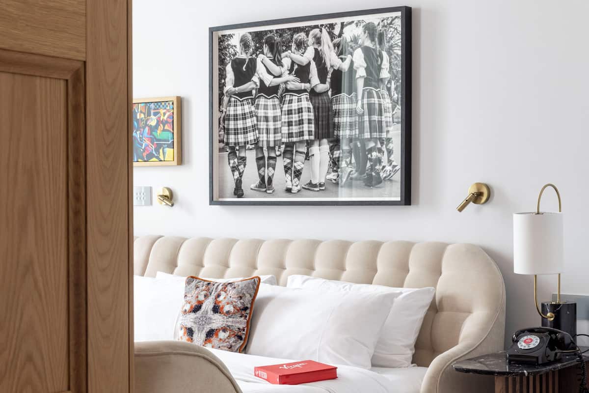A bedroom with a bed, a framed picture on the wall, a bedside lamp, and a small table with a telephone.