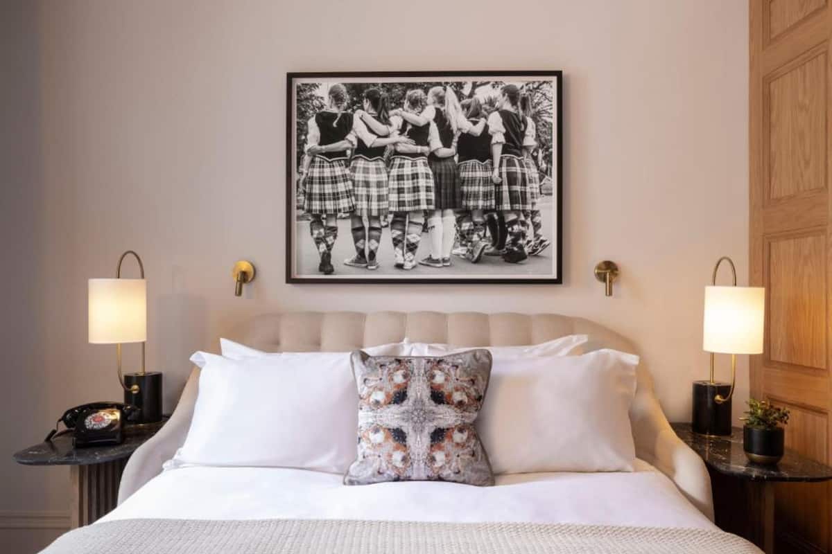 A hotel room with a bed, two bedside tables, a lamp, a framed picture on the wall, and a door.