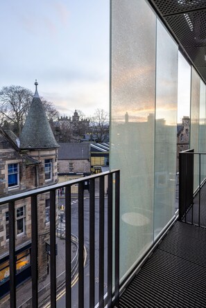 A modern building with large glass windows, a metal railing, and a view of a historic town with a tower.