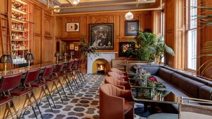 A bar area with red chairs and a long counter, a fireplace with a painting above it, and a seating area with a sofa and tables.