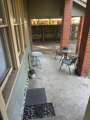 En overdækket terrasse med betongulv, to runde borde og fire stole.